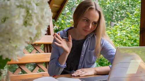 Junge glückliche Frau konzentriert sich auf ihren Laptop in einer Holznische. Die entspannte Umgebung im Freien betont Komfort und Produktivität.