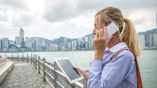 Ausländische Geschäftsfrau am Telefon, mit digitalen Tablet vor der Skyline von Hongkong.