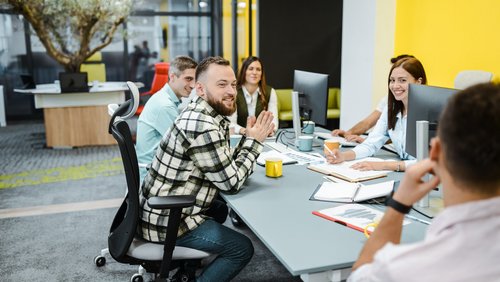 Lächelnder männlicher Projektmanager ermutigt zum Brainstorming während eines Geschäftstreffens mit Kollegen/innen.