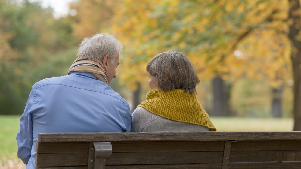 Älteres Paar sitzt auf Parkbank im Herbst. 