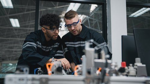 Studentischer Ingenieur montiert Roboterarm mit Computer in der Technologiewerkstatt. Servicetechniker, der die Robotersteuerung hält und die Schweißhardware des Roboterarms überprüft.